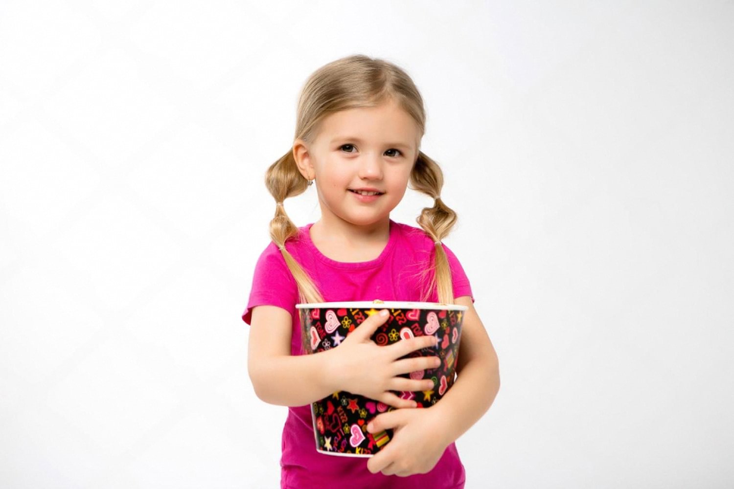 Young girl in a pink shirt holding a large popcorn bucket at a school event