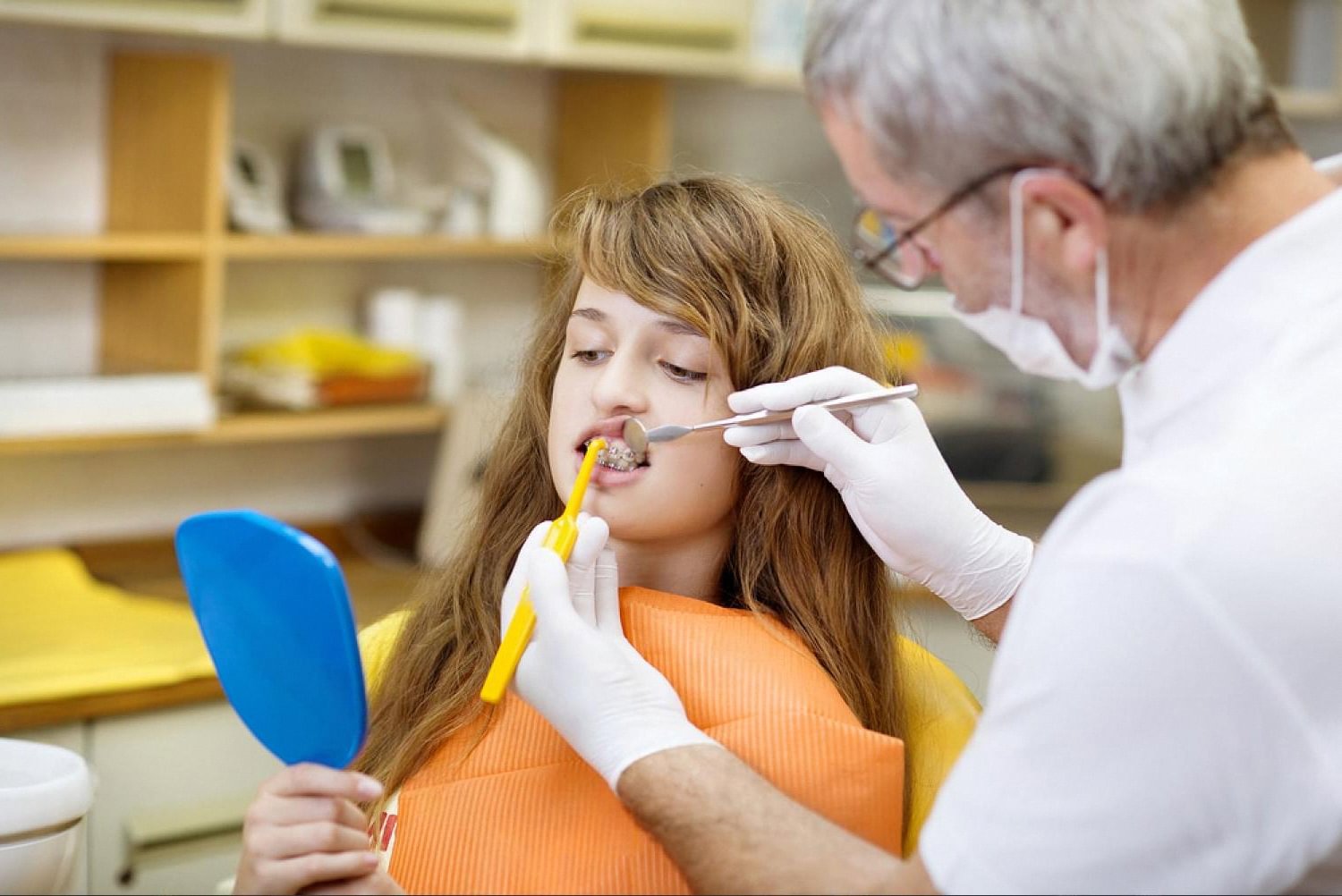 Orthodontist showing a young patient with braces how to clean around brackets during a bite correction visit